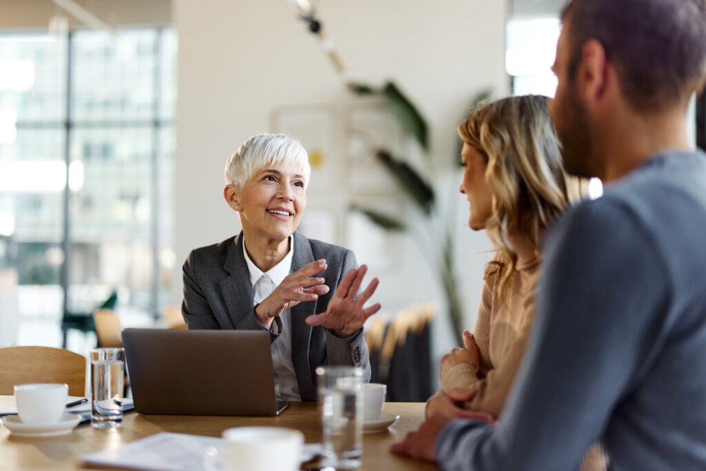 Happy senior real estate agent communicating with a couple during a meeting in the office.